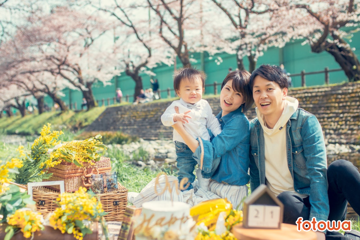 桜の下で笑う夫婦と子どもの誕生日写真