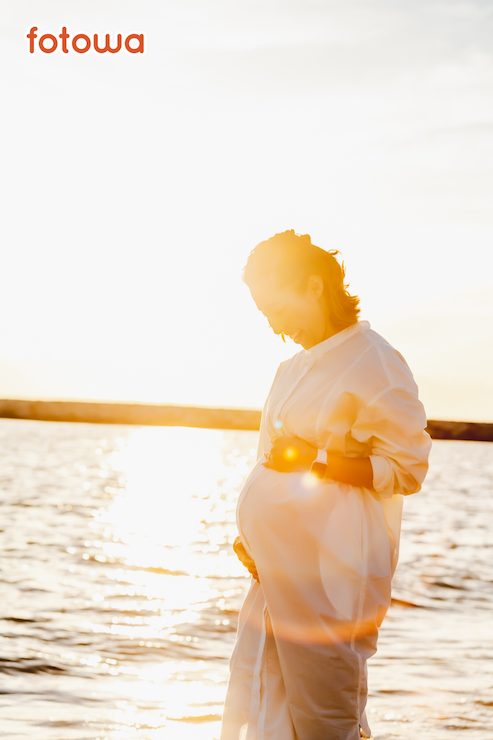 夕日が反射する海岸に立つ女性の美しいマタニティフォトの事例