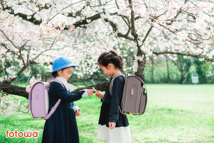 満開の桜の下に立つランドセルを背負った2人の女の子の入学記念写真
