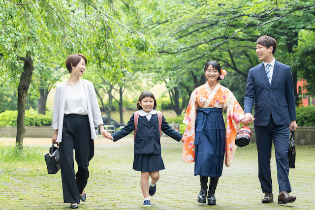 制服・袴・フォーマル服を着た家族が新緑の道を歩いている写真