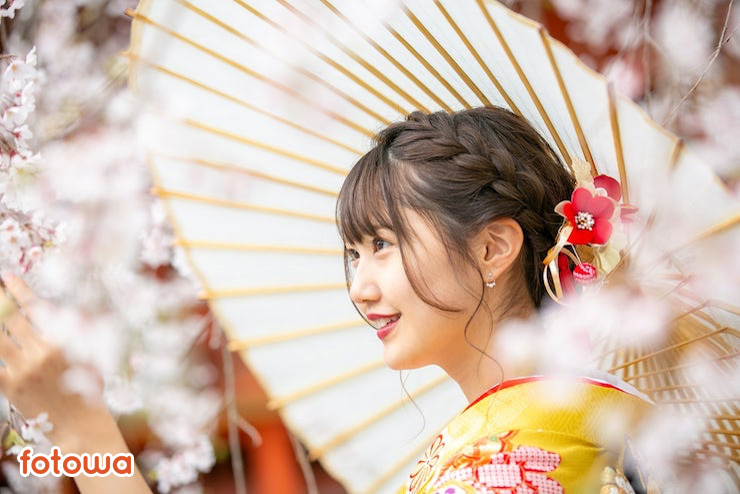 桜を背景に振袖を着た横顔の女性が写る写真